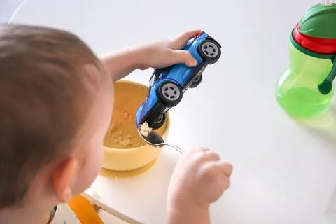 Happy child eats at the table on his own. Healthy food, the child feeds the.. Фото