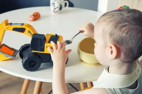 Happy child eats at the table on his own. Healthy food, the boy feeds the c.. Фото