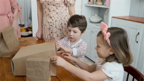 Happy child with gift box. Boy and girl open box with sweets on kitchen morning Stock Footage