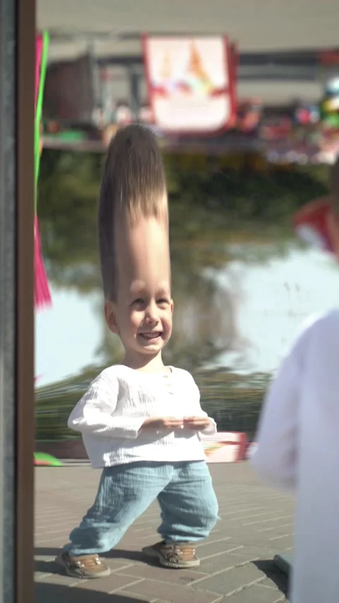 Happy child has fun looking at his distorted reflection in a curved mirror Vidéo 344583296