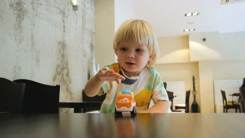 Happy child has fun playing with a colorful car at table in a restaurant Stock Footage 201461156