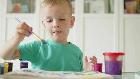 Happy child learning to draw with a brush and paint. Cute blonde boy sittin.. Stock Footage 336182323