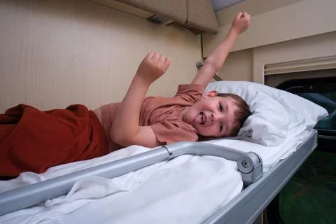 Happy child lying on upper bunk in train compartment. Little boy having fun d Stock Photos