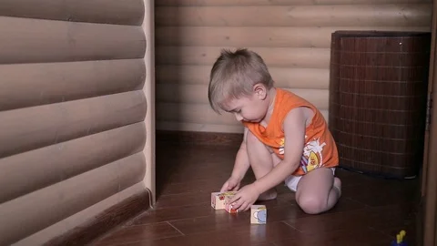 Happy child playing cubes. He wears orange T-shirt, the room has wooden walls Stock Footage 101235367