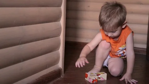 Happy child playing cubes. He wears orange T-shirt, the room has wooden walls Stock Footage 101235513