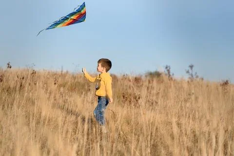 Happy child playing with a kite while running on meadow, sunset, in summer .. Stock Photos