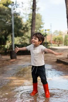 Happy child playing in mud puddle wearing rain boots 库存照片