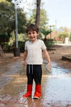 Happy child playing in mud puddle wearing red boots Stock Photos