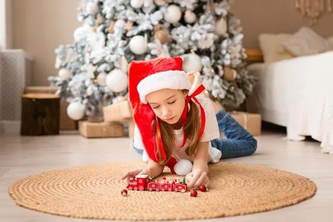 Happy child with red hat playing with toy wood train under christmas tree Stock Photos