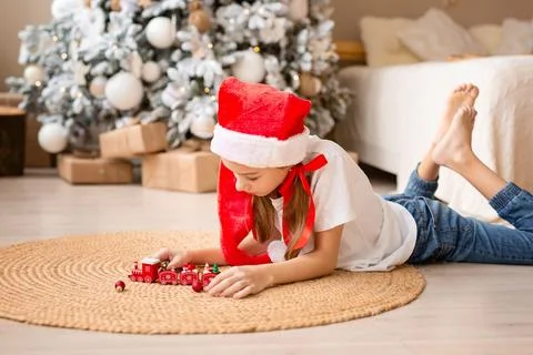 Happy child with red hat playing with toy wood train under christmas tree Stock Photos