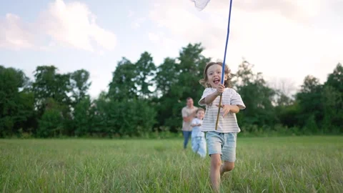 Happy child running through grassy meadow holding butterfly net at sunset. Kid Stock Footage 345958393