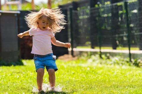 Happy child running through wet lawn splashinh water. Stock Photos
