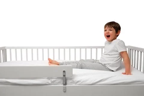 Happy child sitting on bed with security rail isolated on white background. L Stock Photos