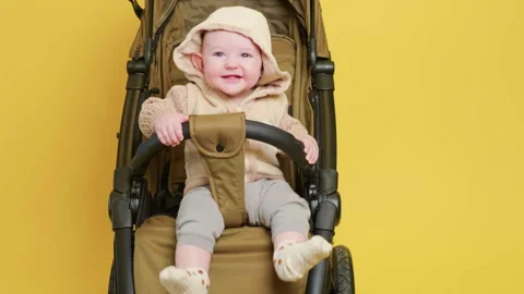 Happy child sitting in stroller on yellow background. Small baby in warm Stock Footage 337418696