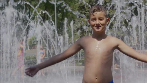Happy child smiling to camera while being sprayed with water sprinkles after Stock Footage 137218280