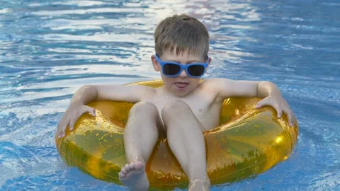 Happy child splashes clear blue swimming pool water with energetic kicks while 库存影片 345654330