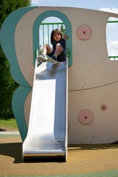 Happy child using playground slide during sunny day Stock Photos