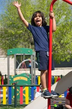 Happy child waving while playing on a slide in a playground Stock Photos