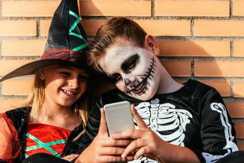 Happy children disguised using the mobile phone in the street. Stock Photos