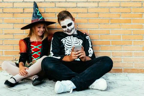 Happy children disguised using the mobile phone in the street. Stock Photos