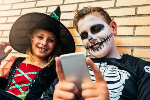 Happy children disguised using the mobile phone in the street. Stock Photos
