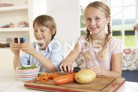 Happy children peeling vegetables in kitchen Stock Photos