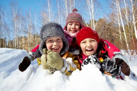 Happy children in winterwear laughing while playing in snowdrift outside Stock Photos
