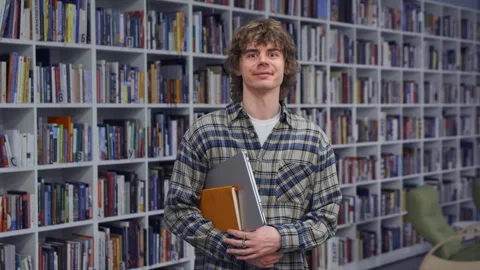 Happy College Guy Posing with Laptop and Notebook Before Library Bookshelf Vídeo Stock 335141411