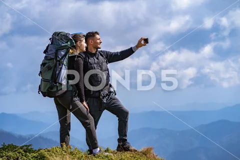 The happy couple with backpacks take a selfie on the cliff Stock Photos