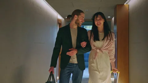 Happy couple with baggage walking in corridor looking for hotel room. Smiling Stock Footage 252141226