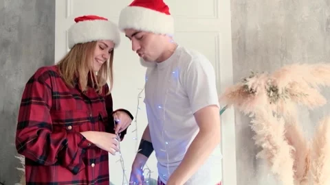 Happy couple bouncing on the bed with Christmas lights at home wearing hats 動画素材 145496422
