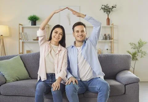 Happy couple celebrating relocation making hand roof above heads sitting on sofa Fotos Stock