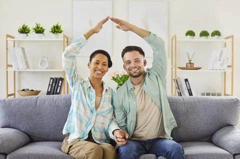 Happy couple celebrating relocation making hand roof above heads sitting on sofa Fotos Stock