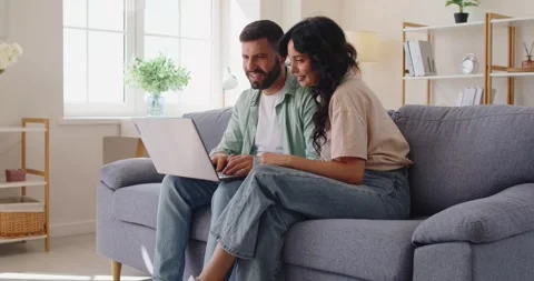 Happy couple on couch using laptop at home, browsing and planning online 库存影片 333018516