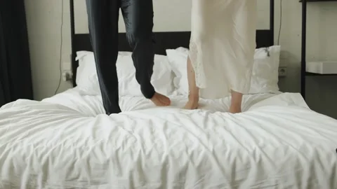 Happy couple dancing on bed, close-up of legs. Jumping and laughing together Stock Footage 323376733