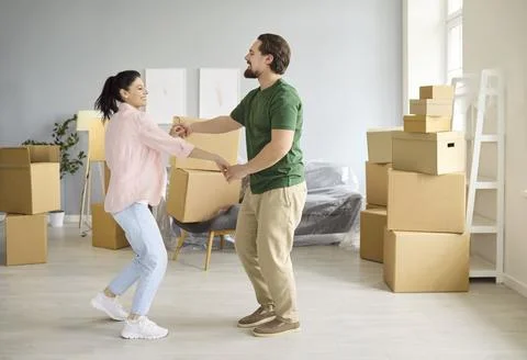 Happy couple dancing with moving boxes in new home, celebrating relocation Stock Photos
