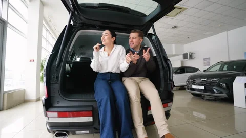 Happy couple dancing while sitting in new car trunk Stock Footage 303384003