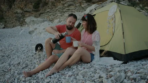 Happy Couple drinking tea on pebble beach with Adorable dog Video stock 138462488