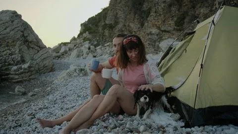 Happy Couple drinking tea on pebble beach with Adorable dog breed king charles Stock Footage 138463695