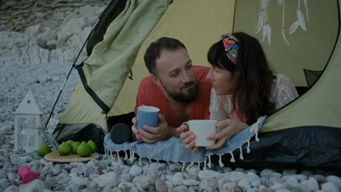 Happy Couple drinking tea on pebble beach and  lie in tent Stock Footage 138483535