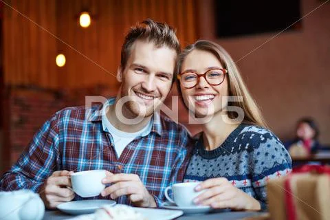 Happy couple with drinks looking at camera in cafe Stock Photos