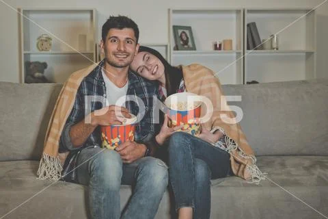 The happy couple eating popcorn and watch movie on the sofa Stock Photos