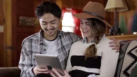 Happy Couple Enjoy Using Tablet Together On Couch, In Cozy Cabin Video stock 73007720
