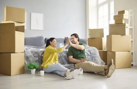 Happy couple high five while moving into new home, celebrating teamwork success Stock Photos