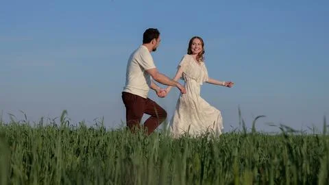 Happy couple holding hands while running through tall green meadow under clear Fotos Stock