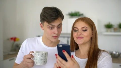 Happy couple at home in kitchen at breakfast using smartphone together browsing Video stock 86185953