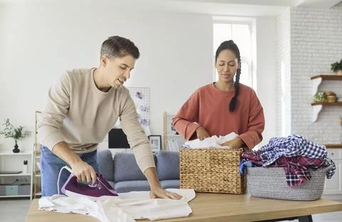 Happy couple ironing laundry and sorting clothes together at home, teamwork Photos