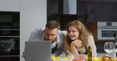 Happy couple in kitchen cooking dinner using laptop computer. Stock Footage 147046182