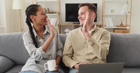 Happy couple laughing on sofa while using laptop and chatting at home indoors Stock Footage 341668166