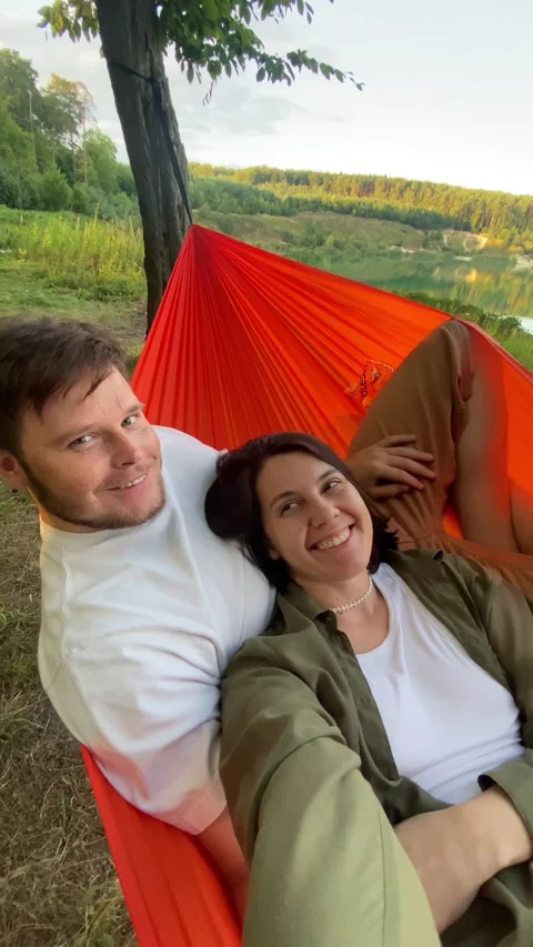 Happy couple laying down in hammock looking on sunset above the lake Video stock 220017417